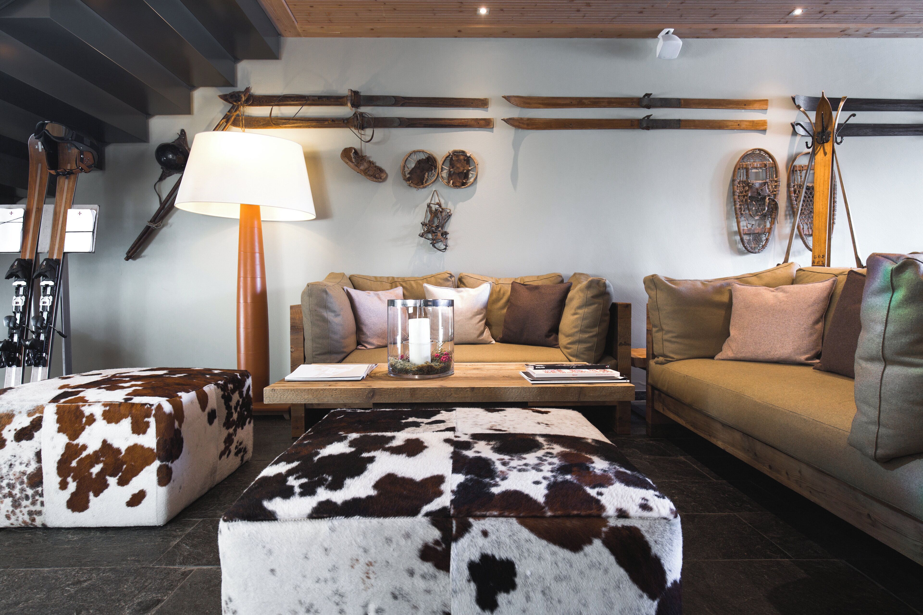 A cozy living room with a sofa, two ottomans, a coffee table, and skis and snowboards on the wall.