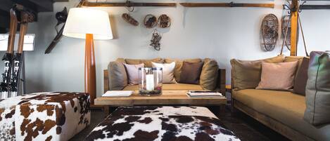 A cozy living room with a sofa, two ottomans, a coffee table, and skis and snowboards on the wall.