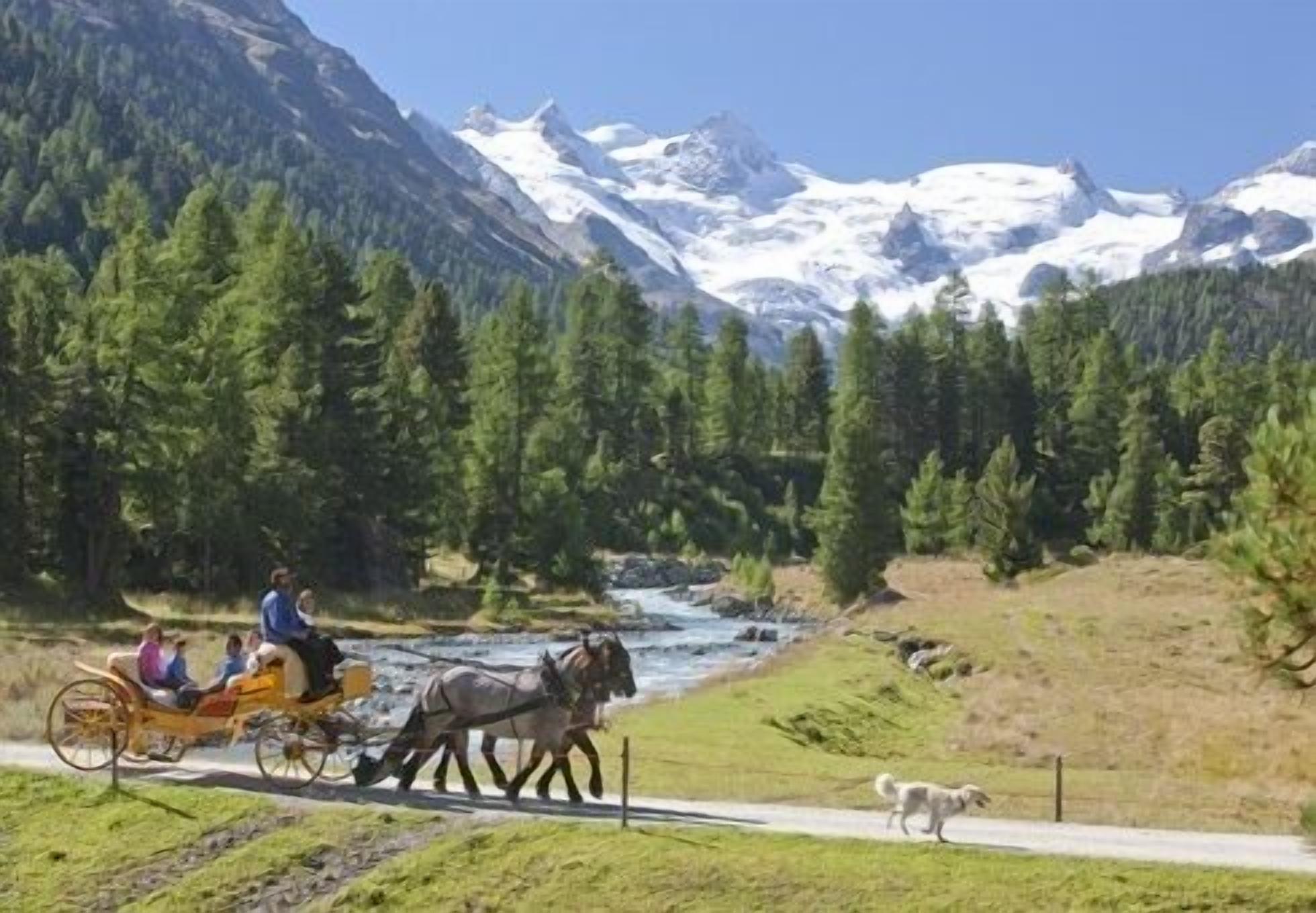 A horse-drawn carriage on a road with a river and mountains in the background.