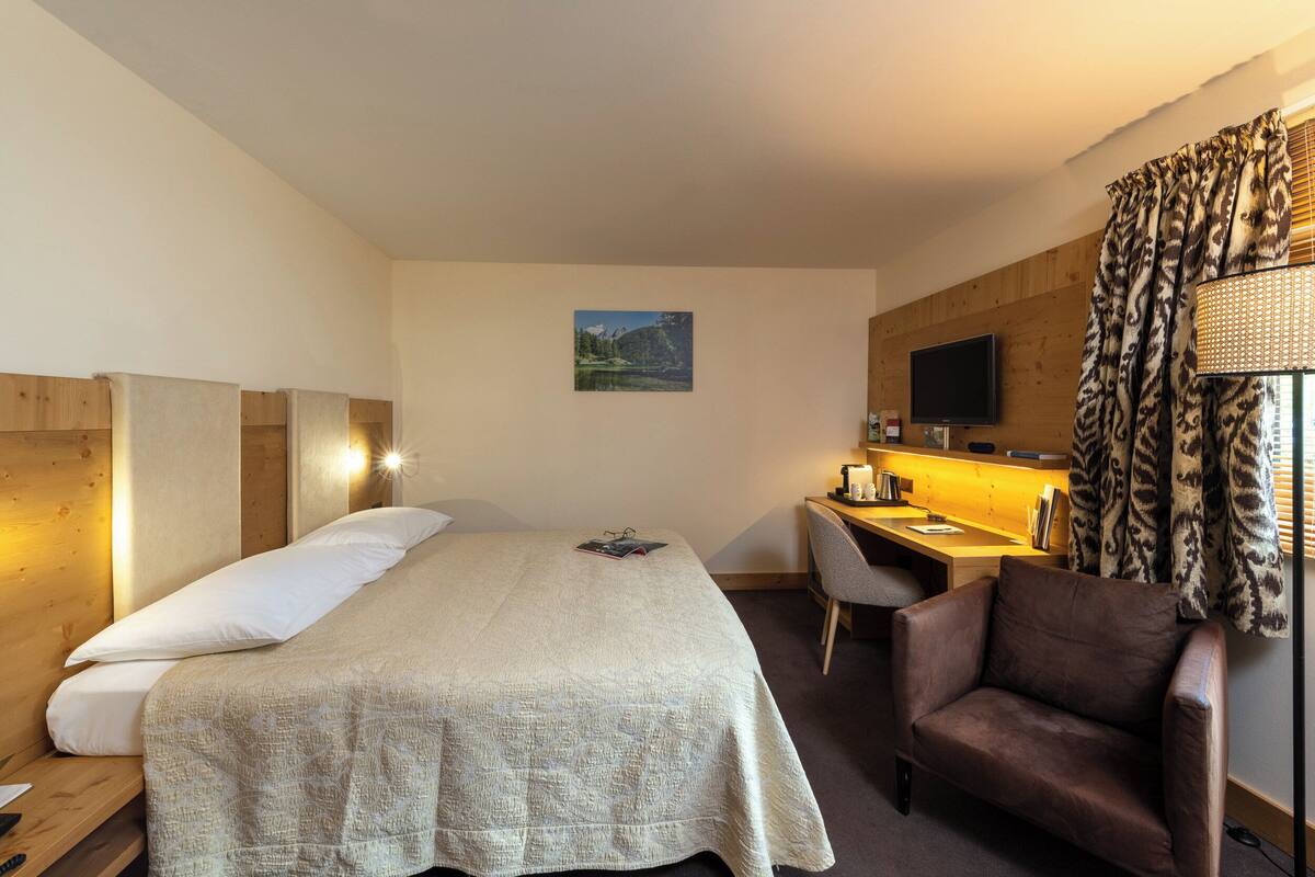 Een hotelkamer met een bed, een bureau, een stoel, een televisie en een raam met gordijnen.