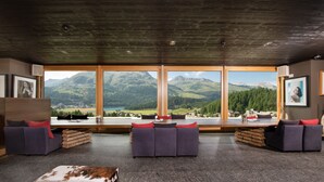Une pièce spacieuse dotée de grandes fenêtres offrant une vue sur les montagnes, d’un ensemble de canapés et d’une table basse en bois.