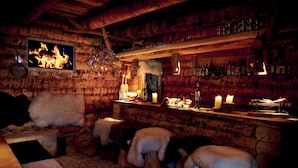 Un intérieur rustique avec des murs en bois, un coin bar avec des bouteilles et des verres, et une cheminée agrémentée de bougies.