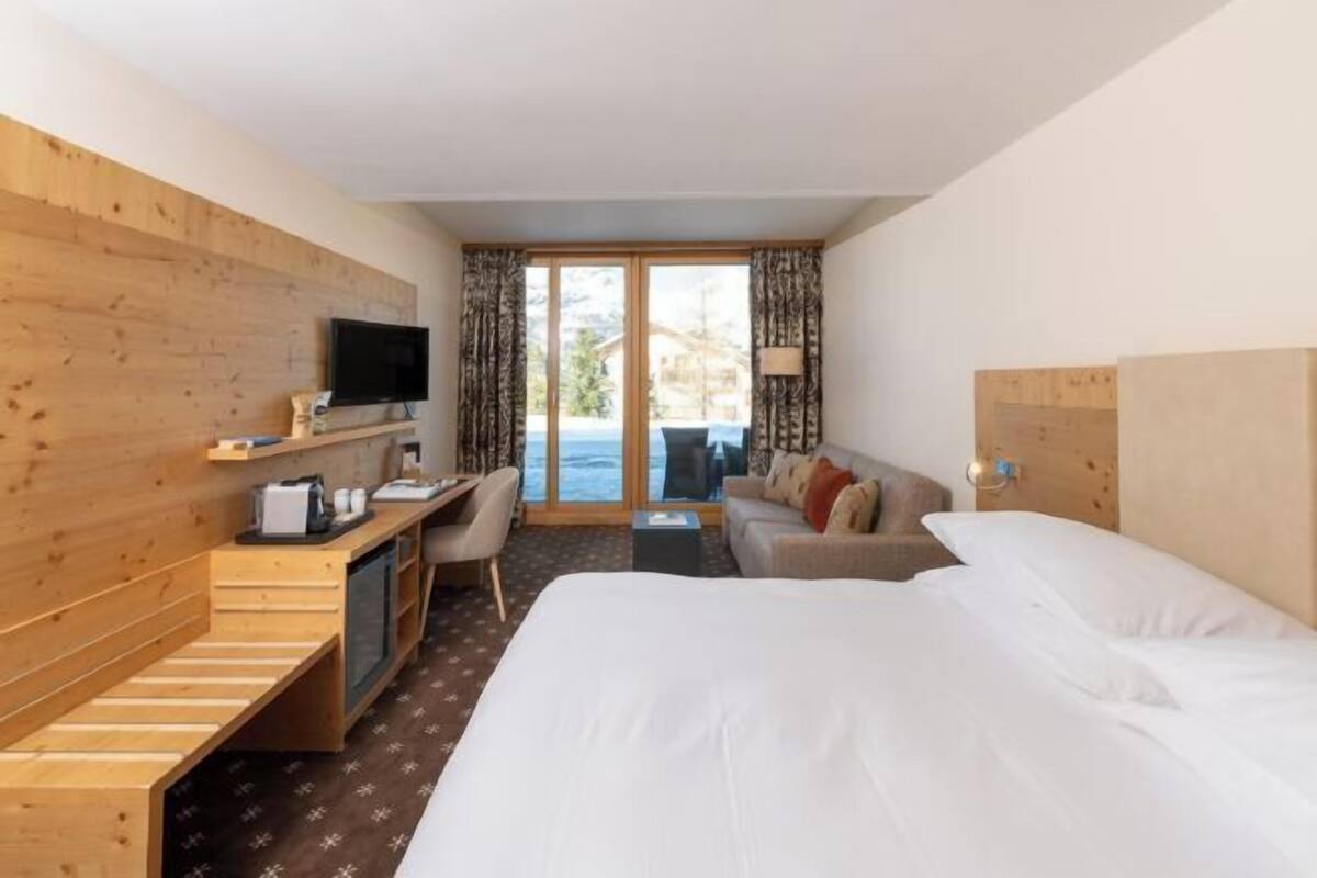 Een hotelkamer met een bed, een bureau, een televisie en uitzicht op het groen.