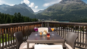 Un balcon avec une table dressée pour deux personnes, offrant une vue sur un paysage montagneux.