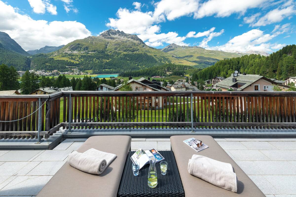 Een balkon met twee lounge fauteuils, een houten omheining en uitzicht op bergen.