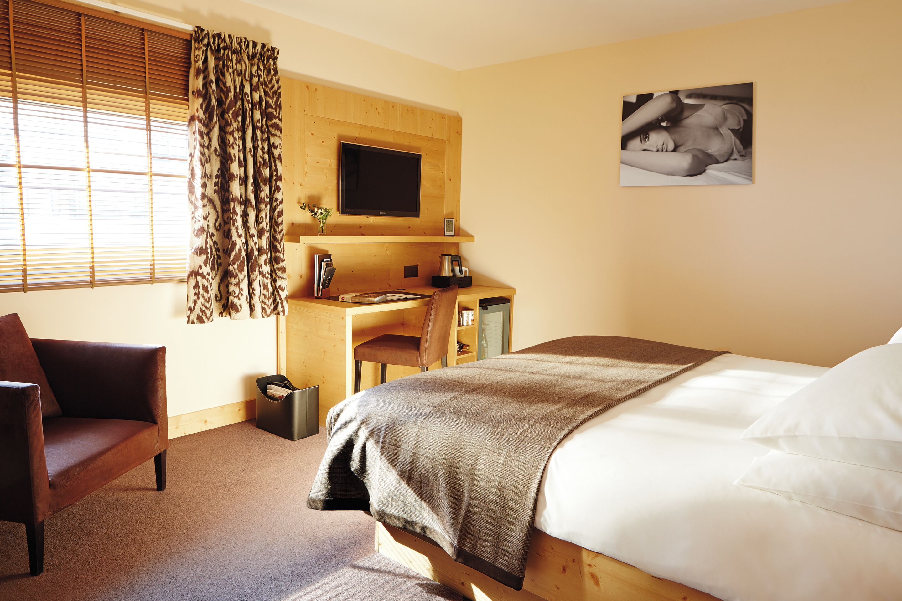 A bedroom with a bed, a desk, a chair, a TV, and a picture on the wall.