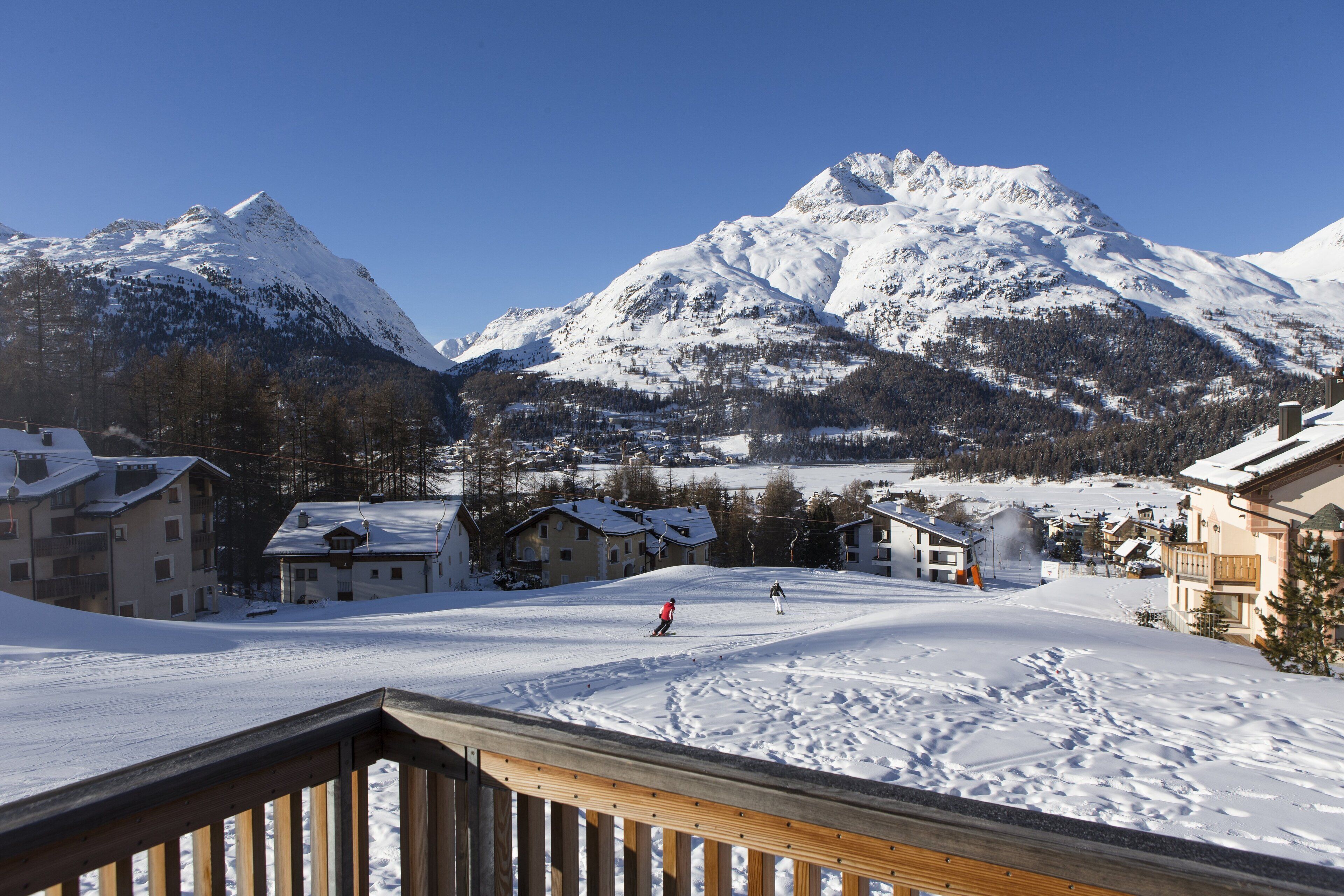 A snow-covered ski resort with buildings, a ski slope, and a mountain in the background.