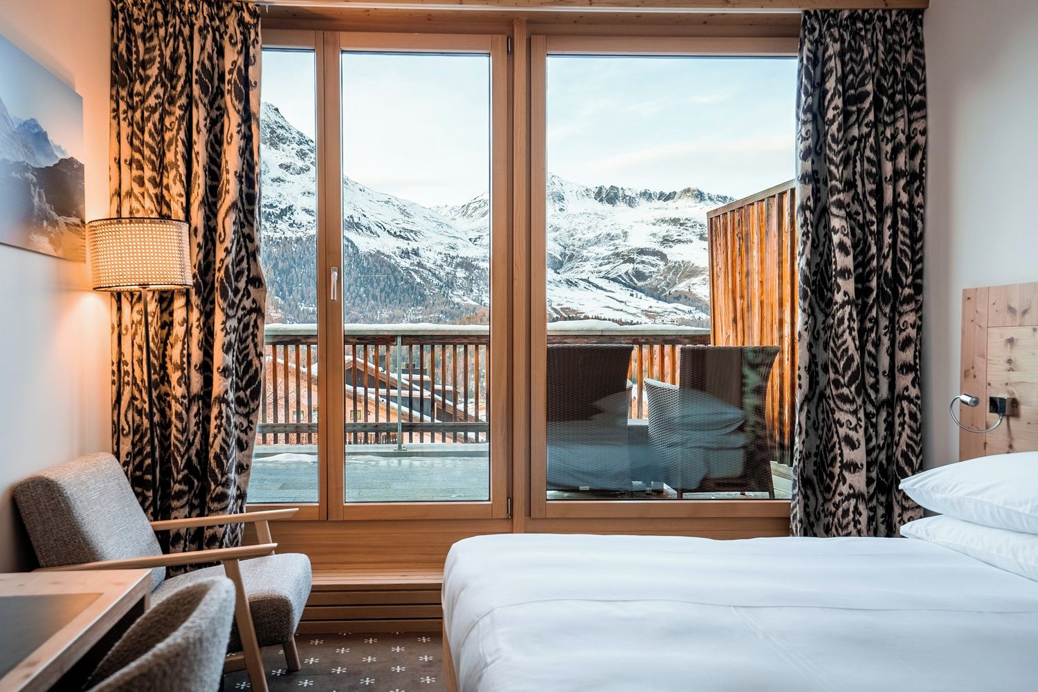 A hotel room with a large window, a bed, a chair, and a small table.