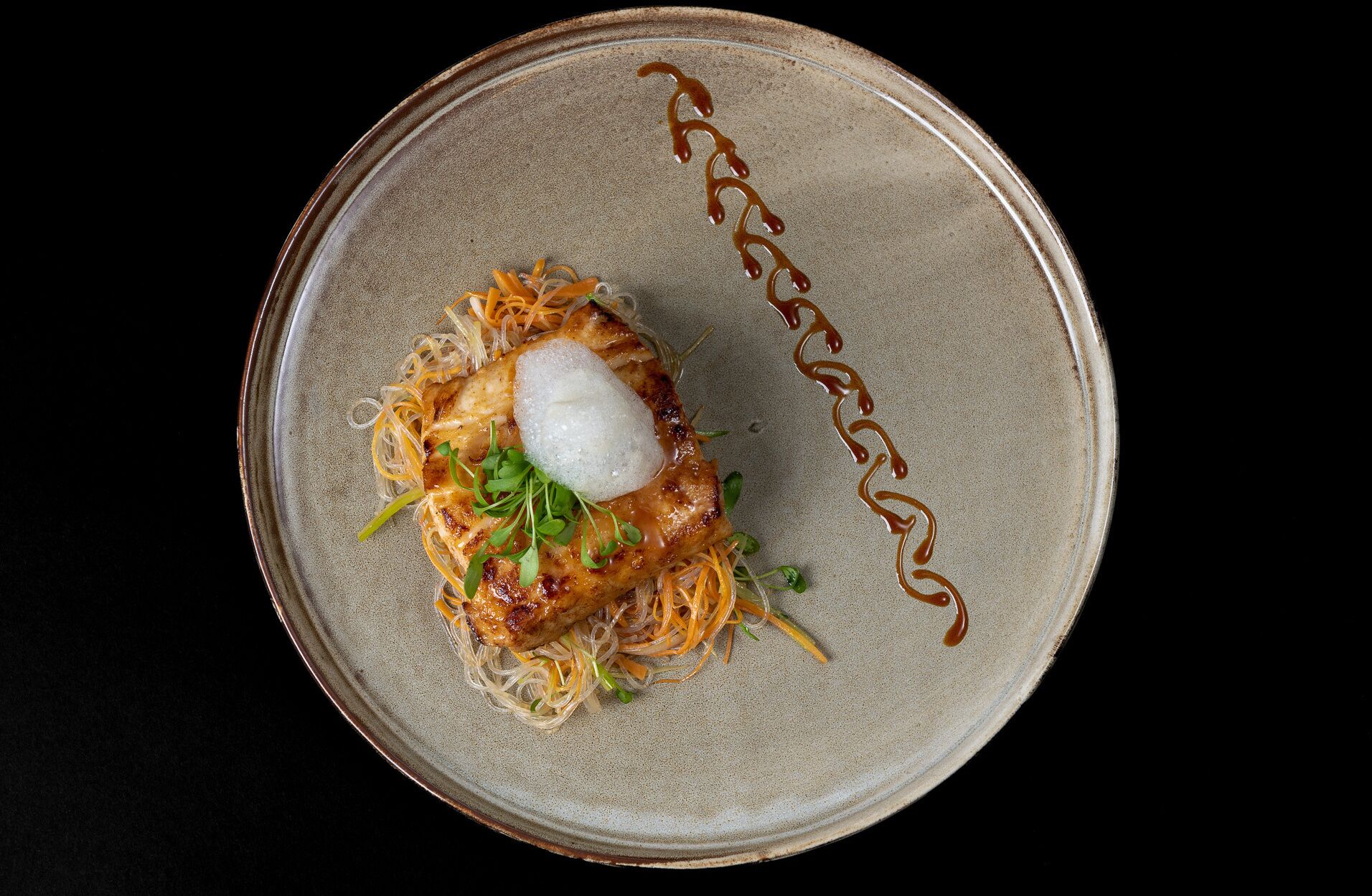 Un plato con un guiso de fideos, un huevo pochado y un chorrito de salsa.