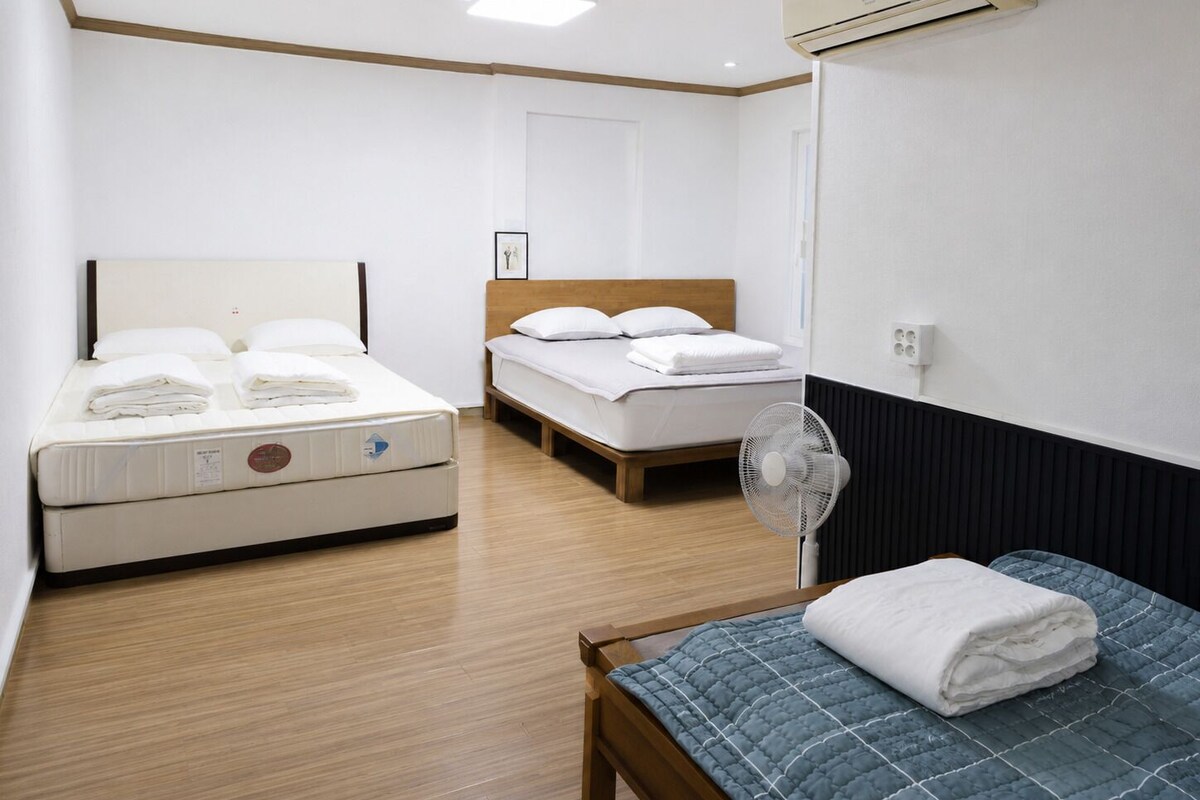 Een hotelkamer met een bed, nachtkastje, ventilator en raam.