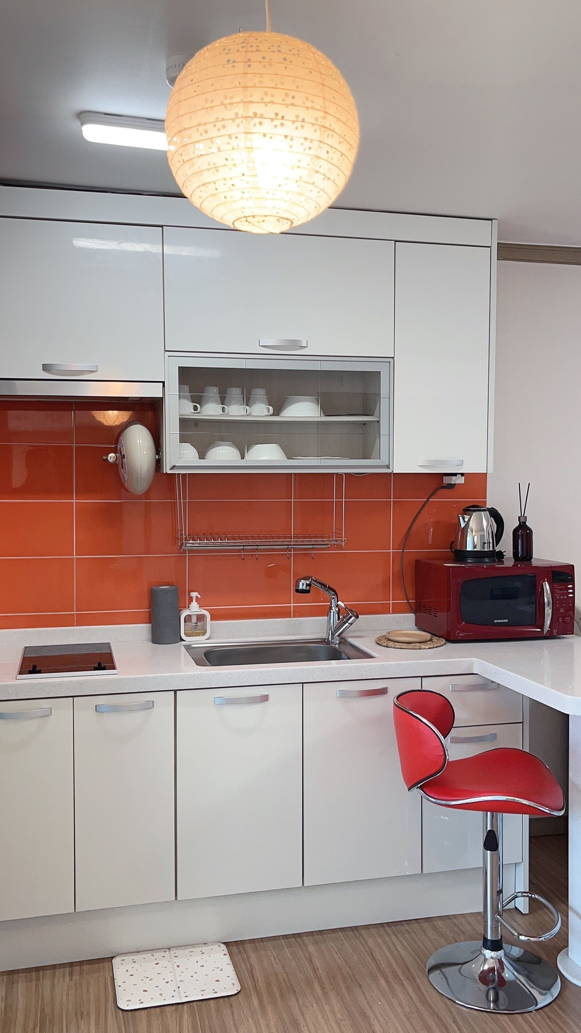 A modern kitchen with white cabinets, a red microwave, a stainless steel sink, and a red bar stool.