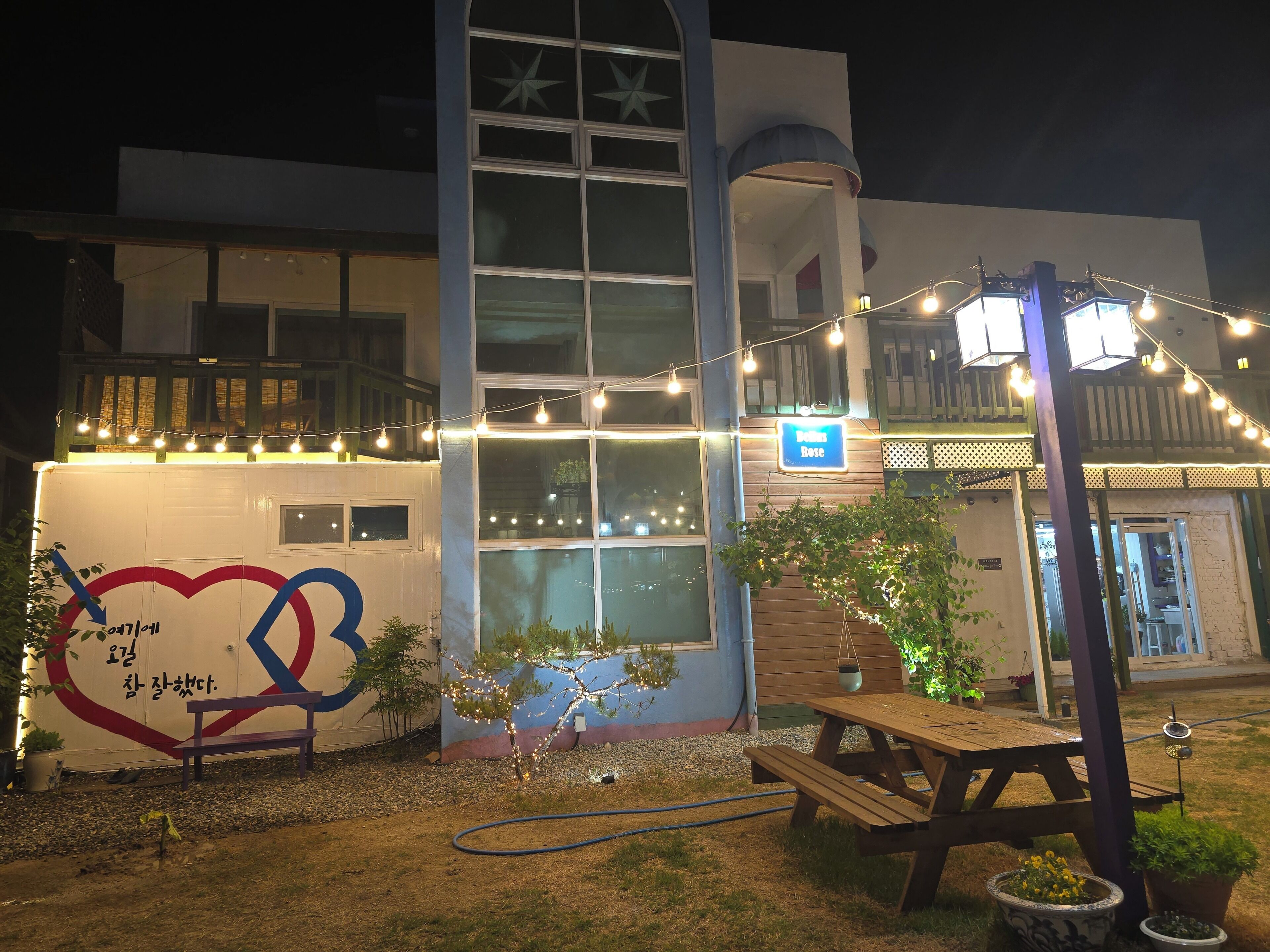 A building with a large window, a bench, a picnic table, and string lights.
