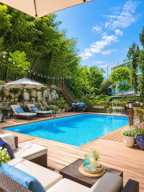A swimming pool with lounge chairs, a wooden deck, and a stone wall. - Bellus Rose Pension Hotel (Gyeongju)