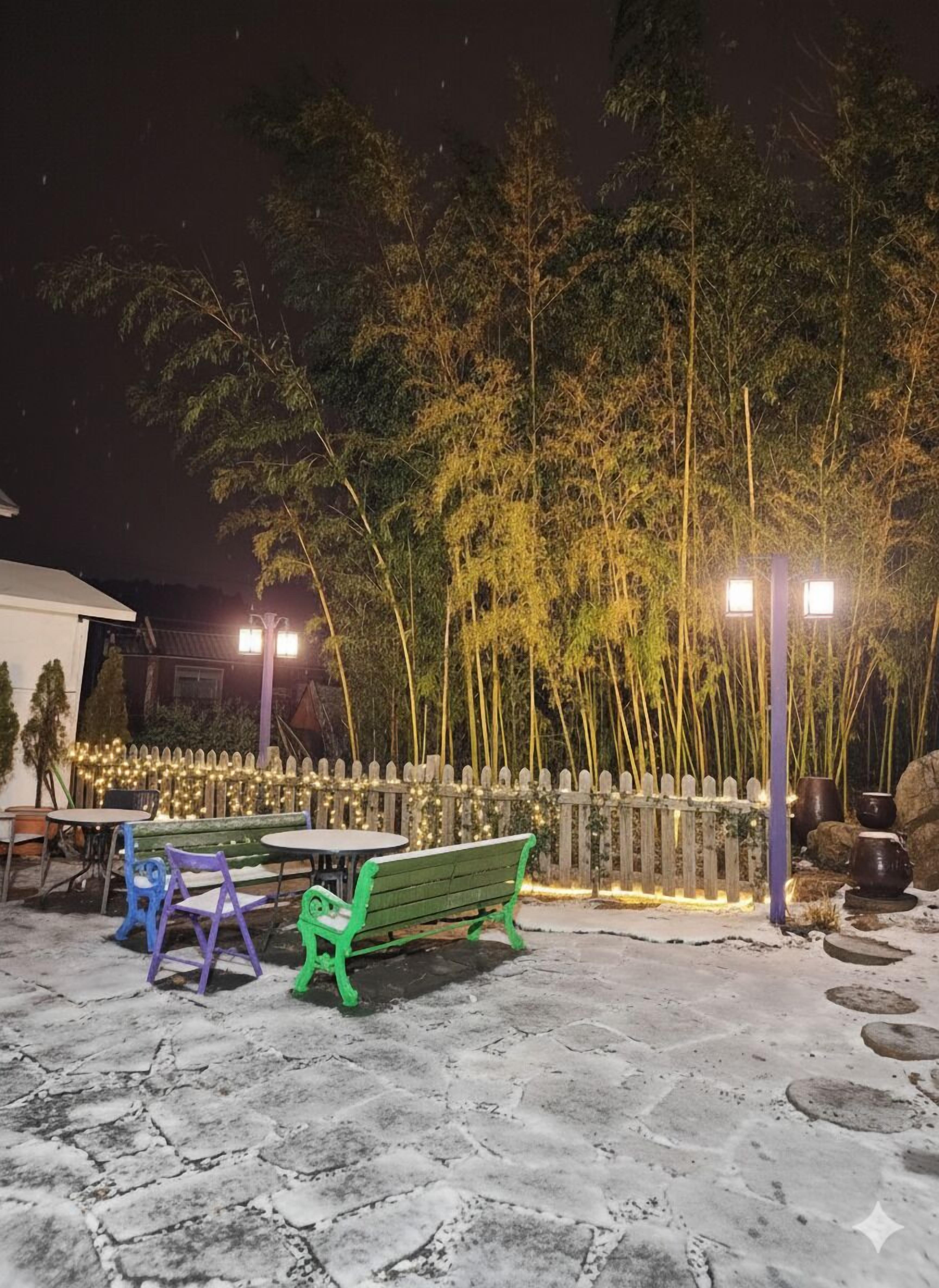 An outdoor seating area with tables and chairs, a wooden fence, and bamboo trees.