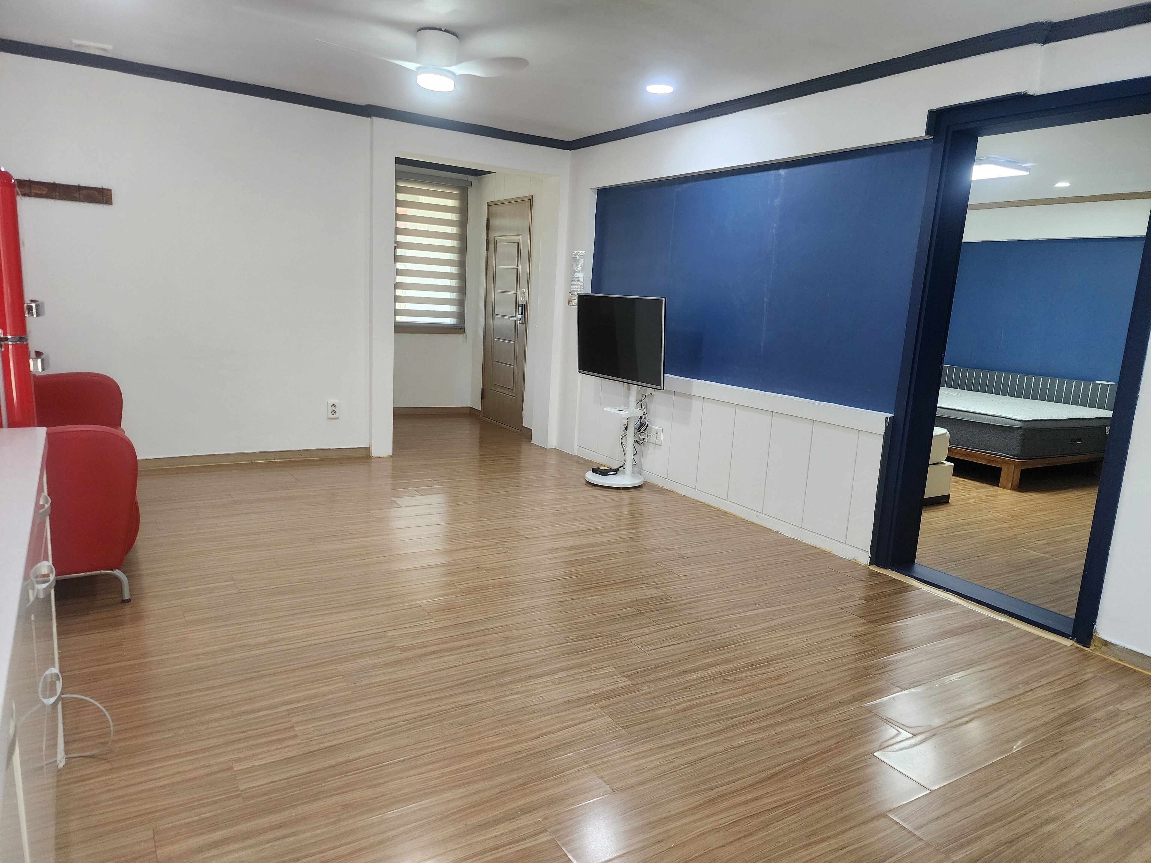 A hotel room with a wooden floor, a large mirror, a bed, a TV, and a red chair.