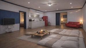 Un salon moderne avec un grand canapé d’angle, un téléviseur à écran plat, un coin cuisine et un canapé rouge en arrière-plan.