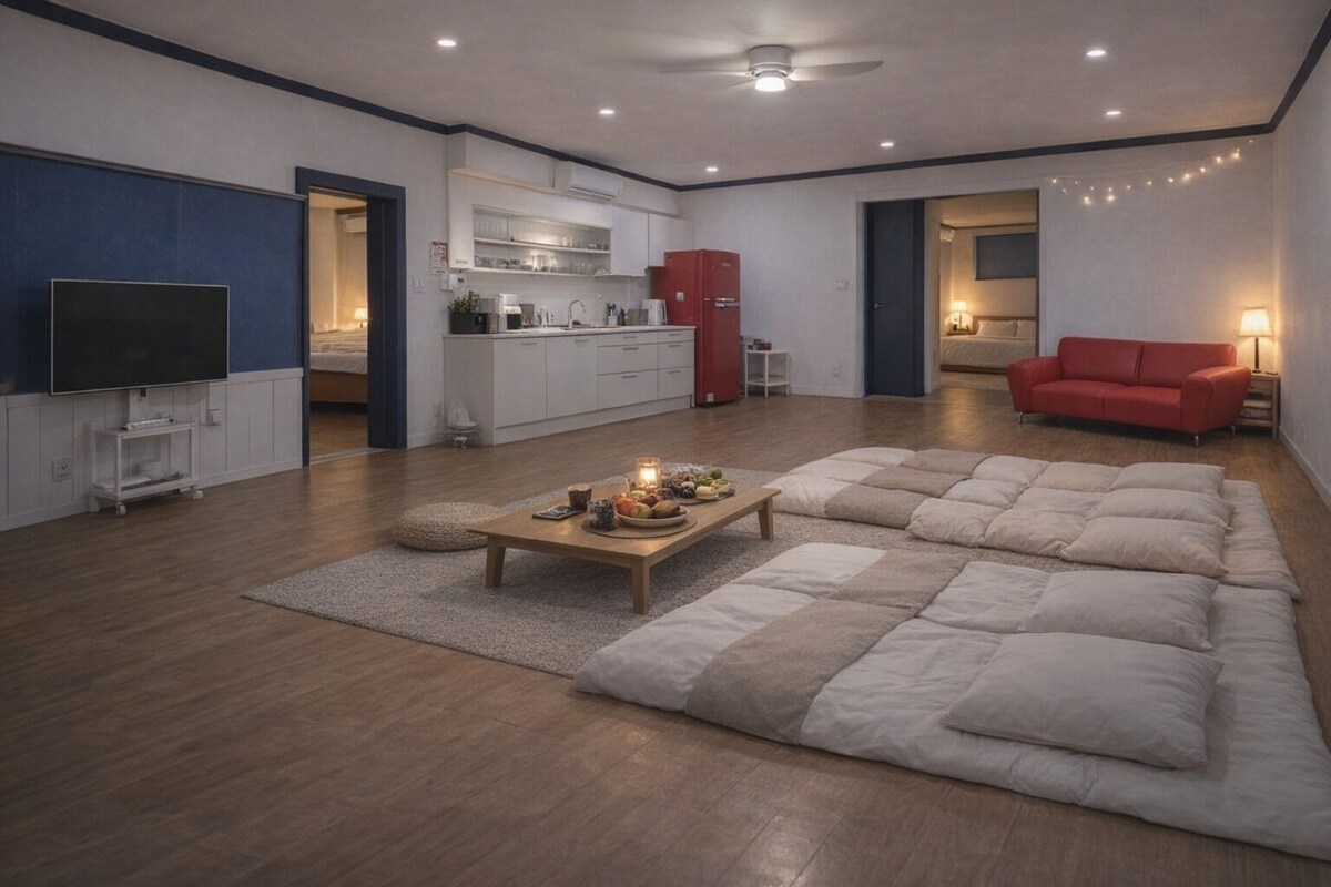 Een moderne woonkamer met een grote hoekbank, een flatscreen televisie, een keukenhoek en een rode bank op de achtergrond.