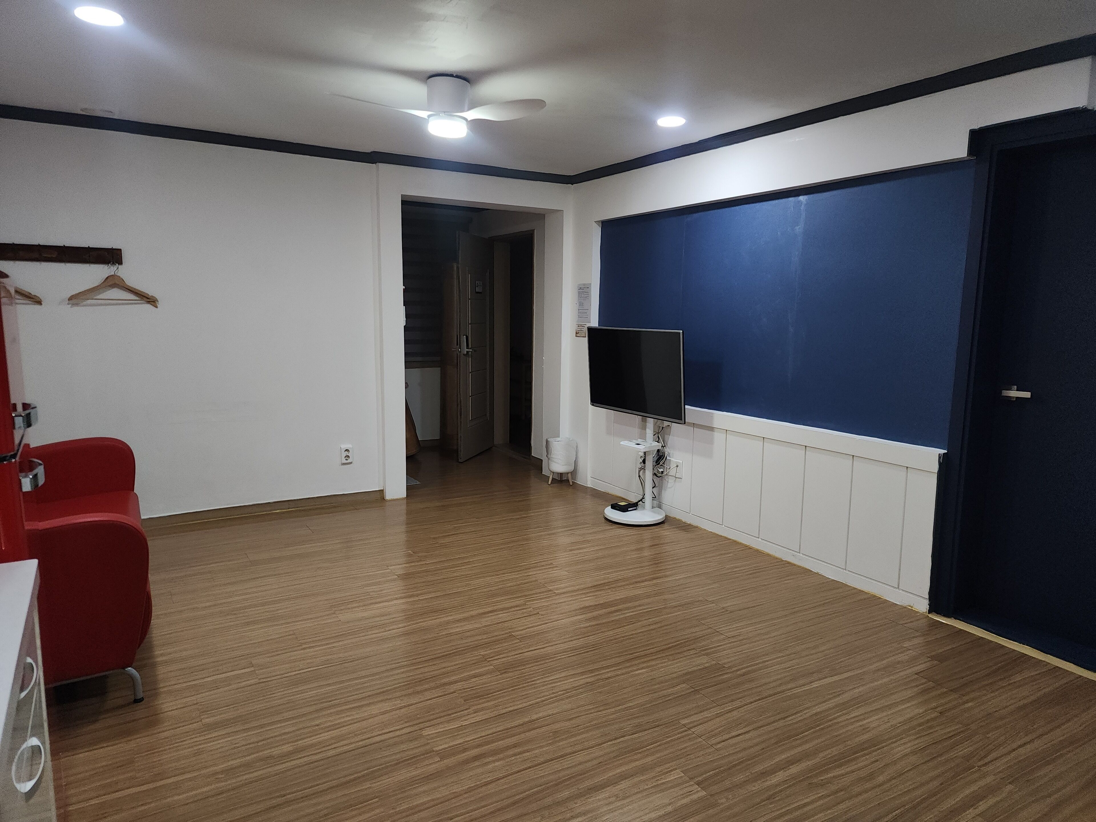 A room with a wooden floor, a ceiling fan, a TV on a stand, a red chair, and a door.