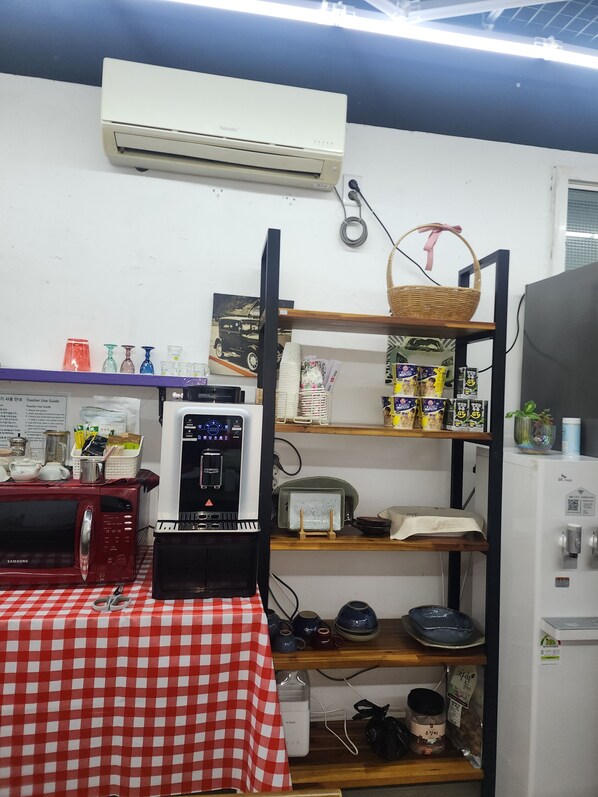 A kitchen with a microwave, toaster, and refrigerator. There is a checkered tablecloth on the table, and various kitchen items are on the shelves.