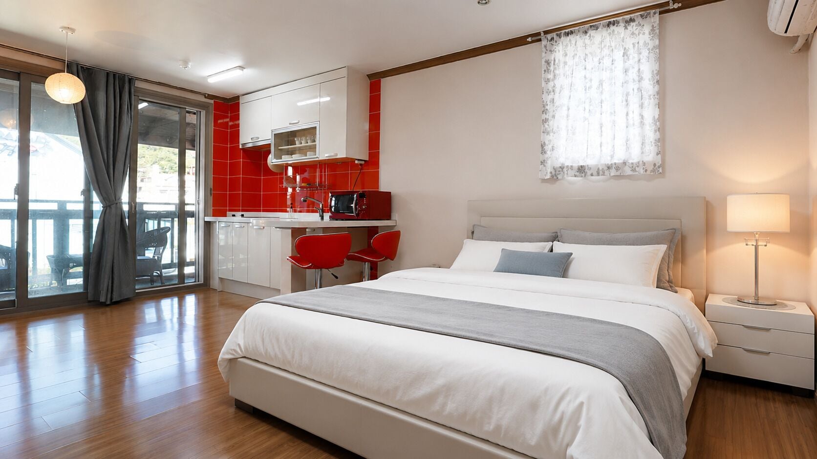 A modern hotel room with a large bed, a separate dining area, and a view through the glass door.