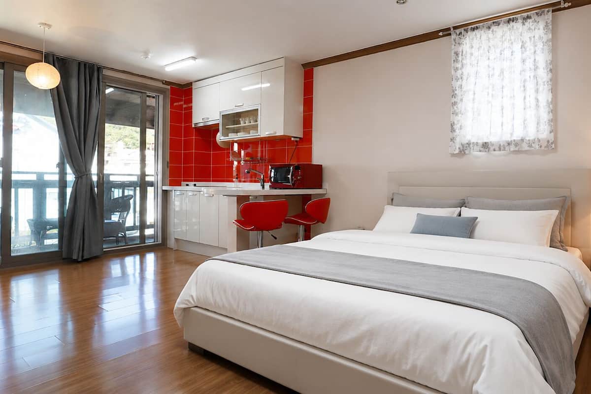 Une chambre d’hôtel moderne avec un grand lit, un coin repas séparé et une vue sur l’extérieur, visible à travers la porte vitrée.