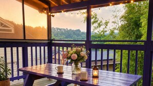 Une terrasse en bois avec une table et des bancs, donnant sur une étendue d’eau et une zone verdoyante.