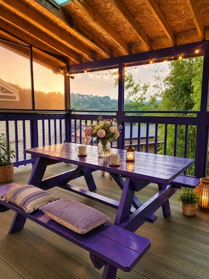 A wooden deck with a table and benches, overlooking a body of water and greenery.