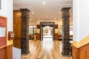 A lobby with marble flooring, ornate pillars, a suggestion box, and a view into the adjacent room.