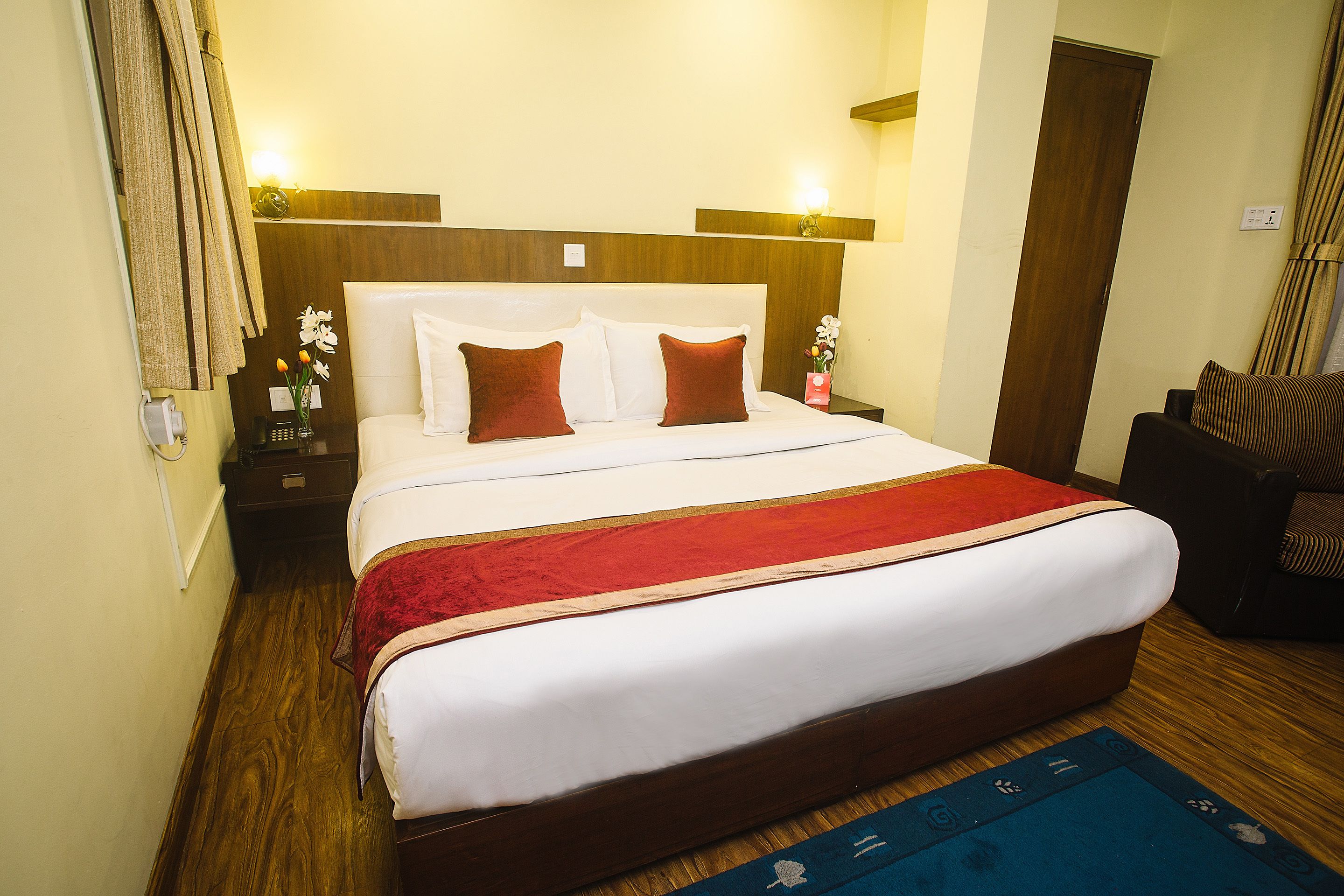 A hotel room with a large bed, wooden headboard, and a red throw blanket.