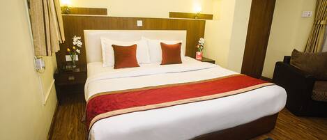 A hotel room with a large bed, wooden headboard, and a red throw blanket.