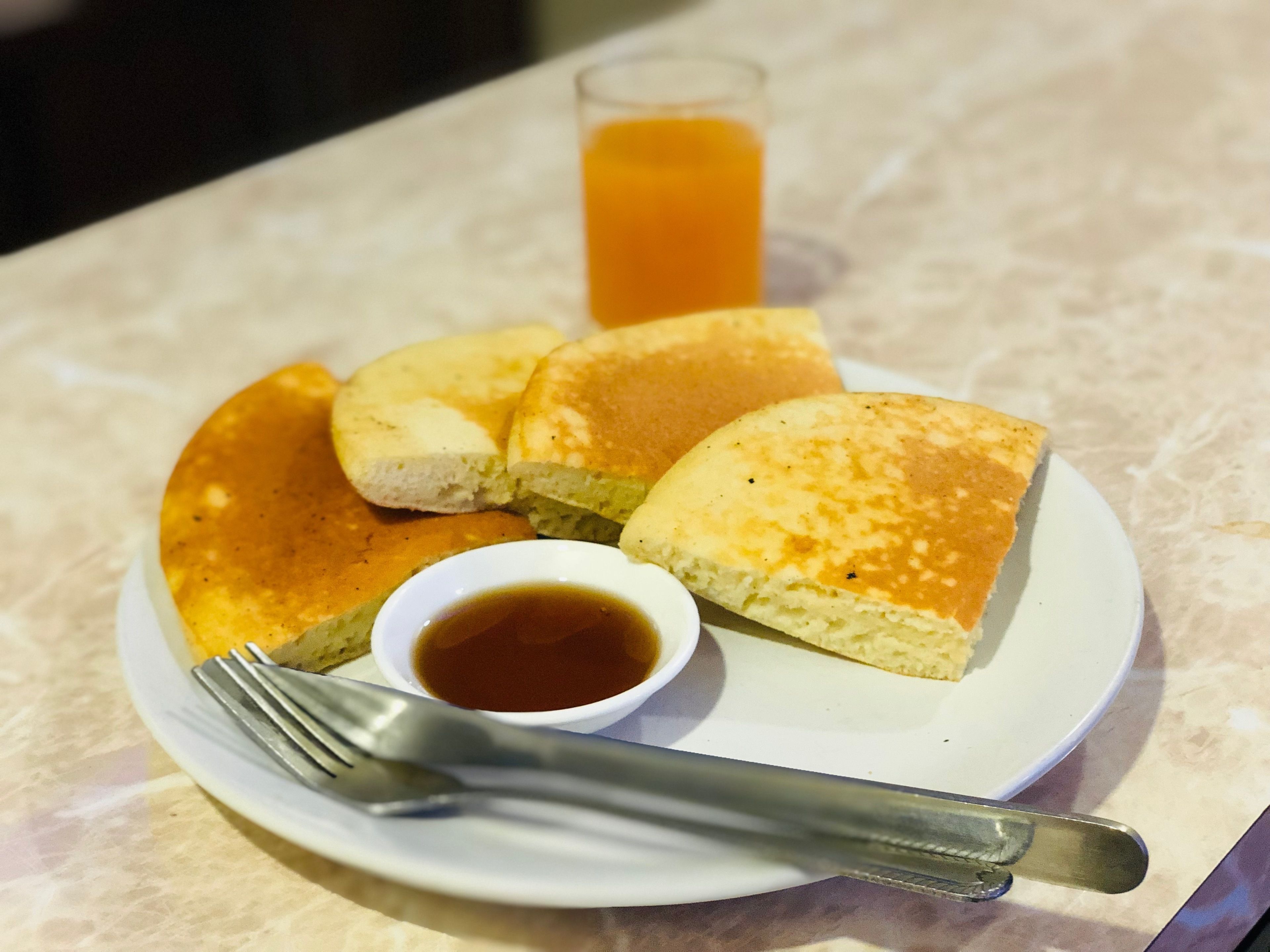 A plate with pancakes, syrup, and a glass of orange juice on a table.