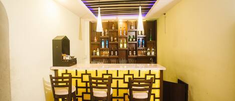 A bar area with a counter and stools, shelves with bottles, and a ceiling with a striped pattern.