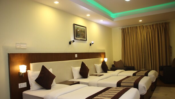 A hotel room with three beds, each with a headboard, bedside lamps, and a framed picture on the wall. - Backyard Hotel (Kathmandu)