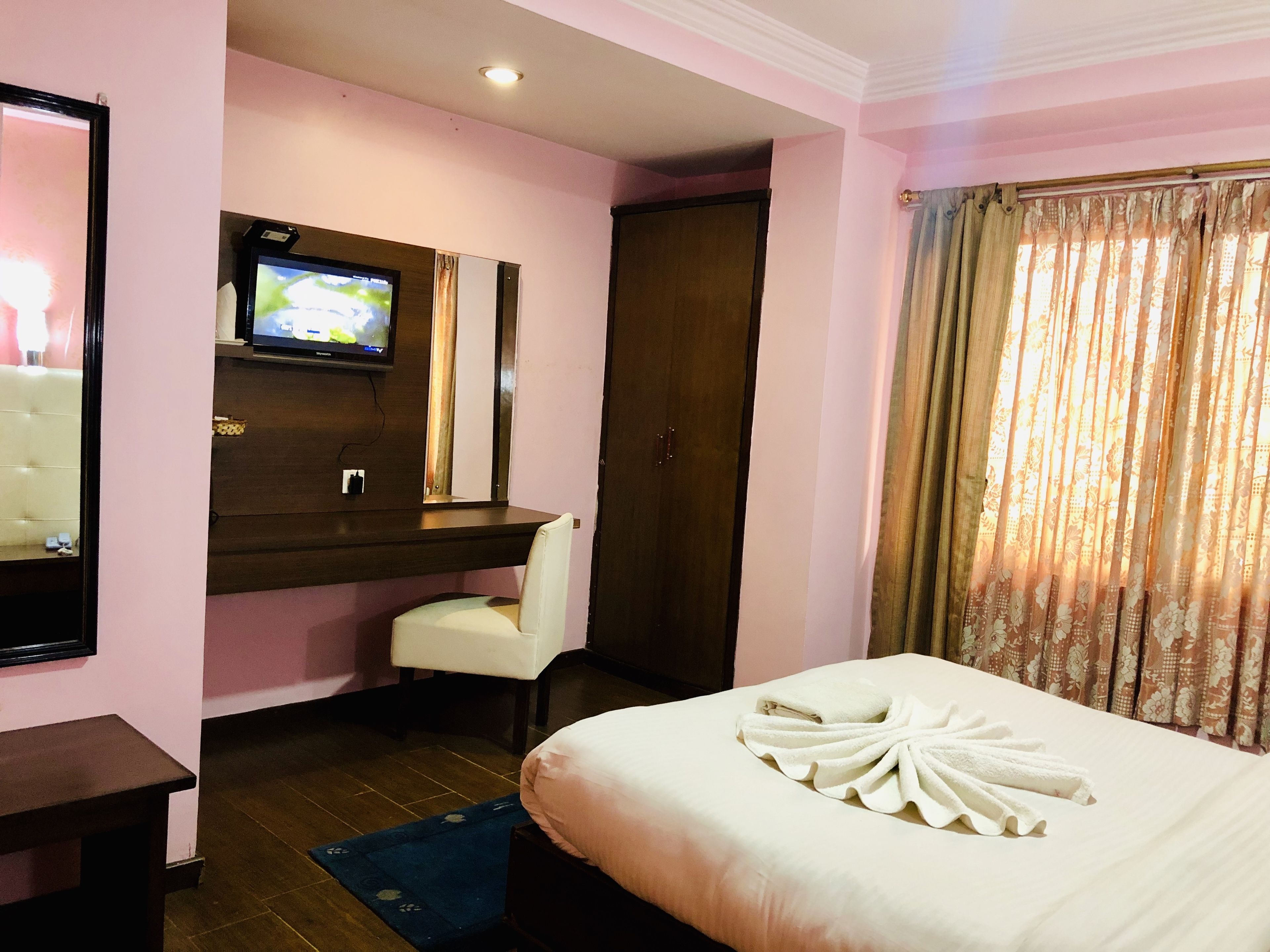 A hotel room with a bed, a TV mounted on the wall, a chair, and a wooden desk.