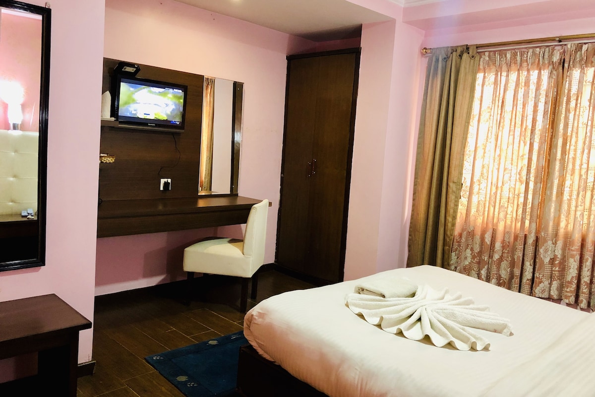 A hotel room with a bed, a TV mounted on the wall, a chair, and a wooden desk.