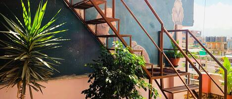 A rooftop terrace with a staircase, potted plants, and a mural.