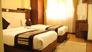 A hotel room with two beds, a wooden wardrobe, a desk, and a window with curtains. - Backyard Hotel (Kathmandu)