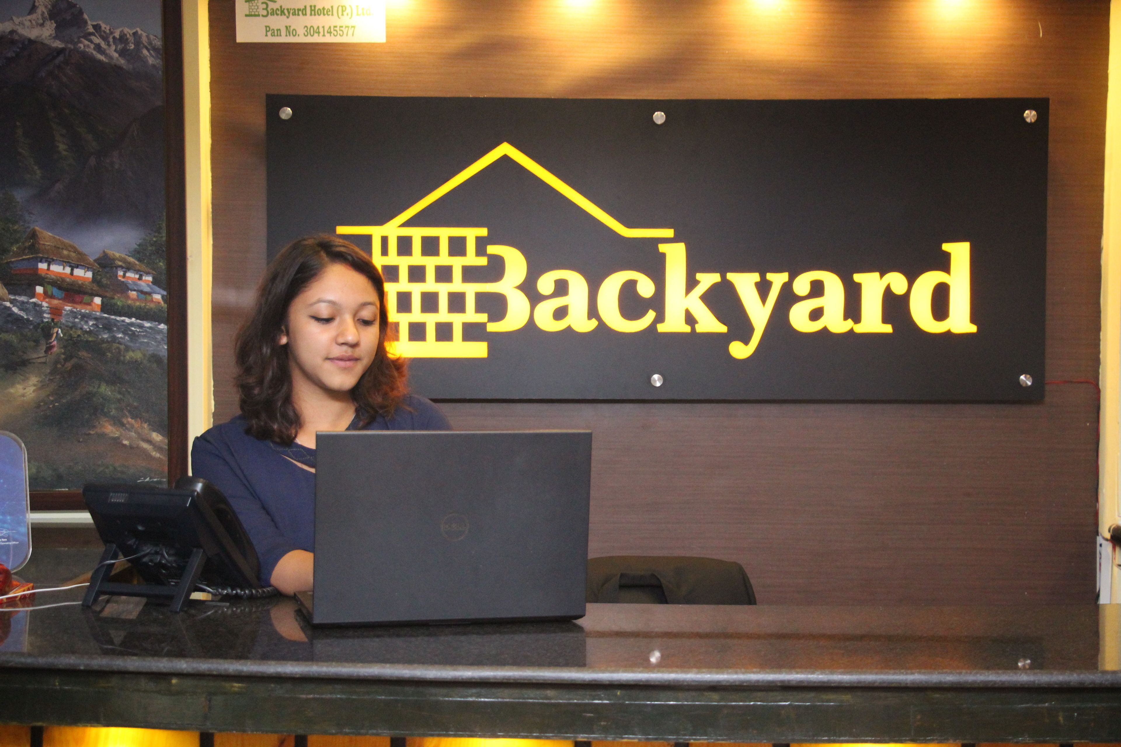 Una mesa de recepción con un cartel que dice "Backyard Hotel" y un ordenador portátil encima.