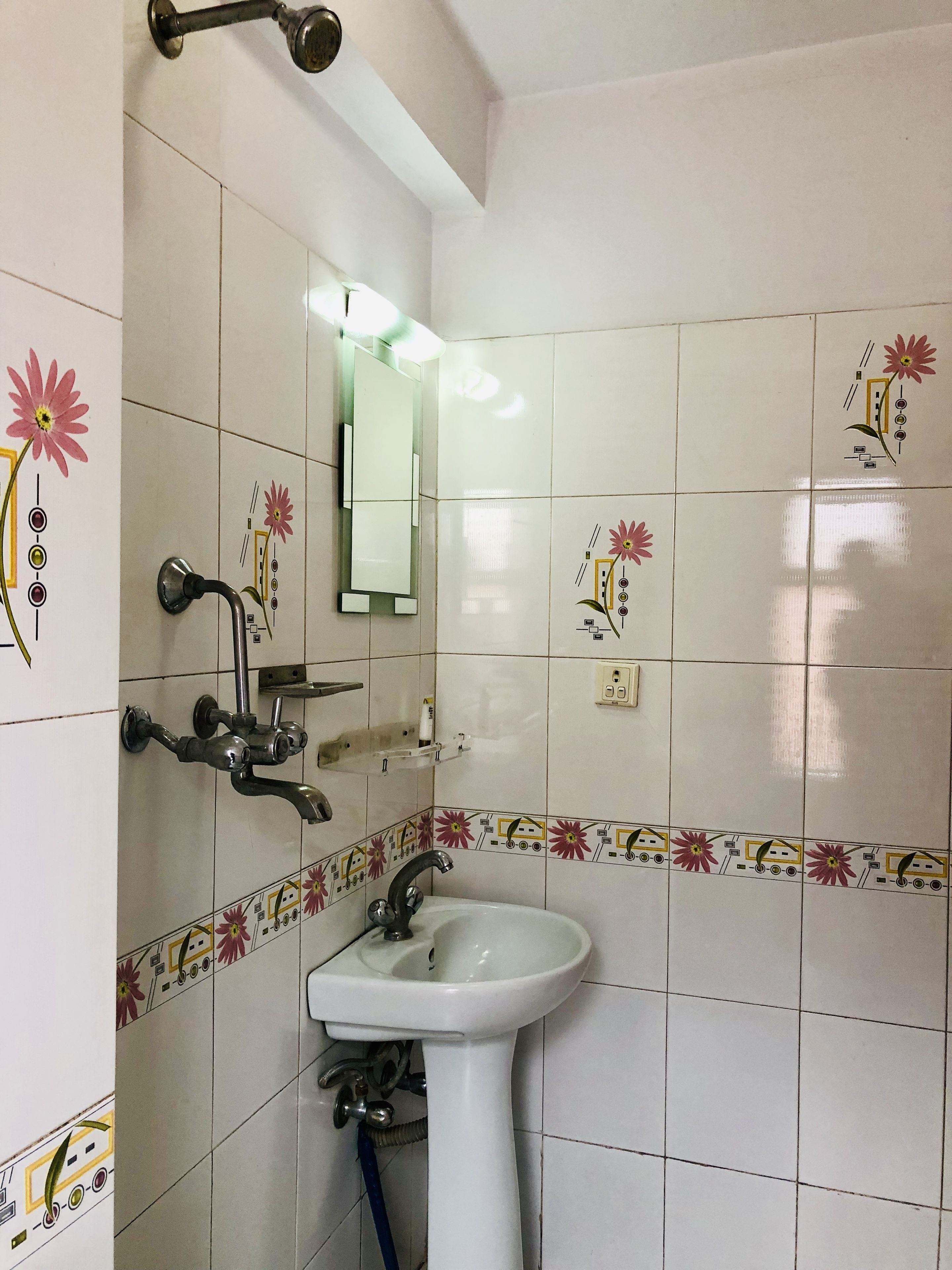 A bathroom with white tiles, a sink, a mirror, and a shower with a handheld showerhead.