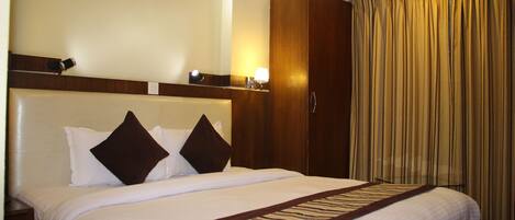 A hotel room with a large bed, a wooden wardrobe, and a curtain.