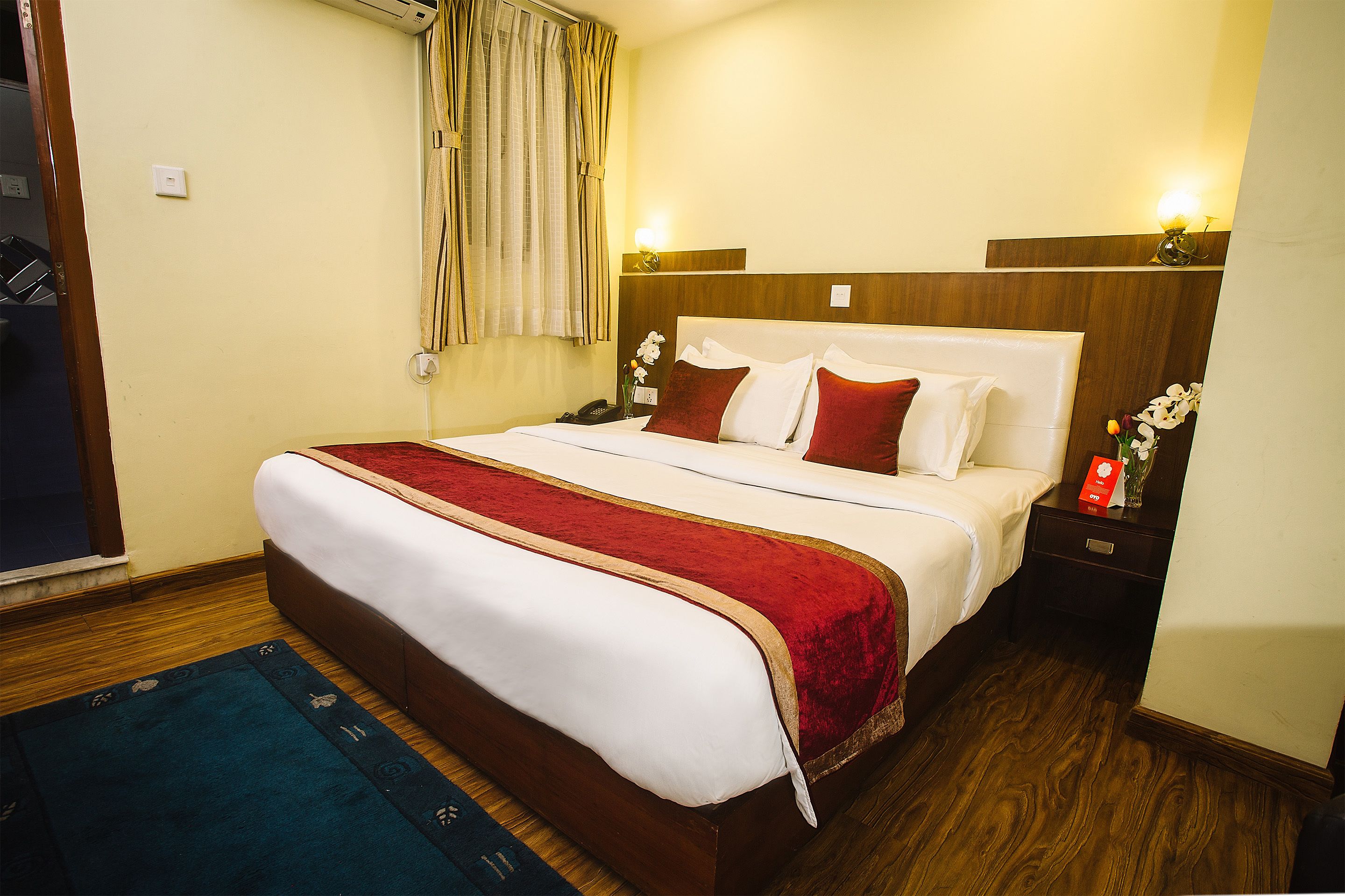 A hotel room with a large bed, wooden headboard, bedside tables with lamps, and a window with curtains.