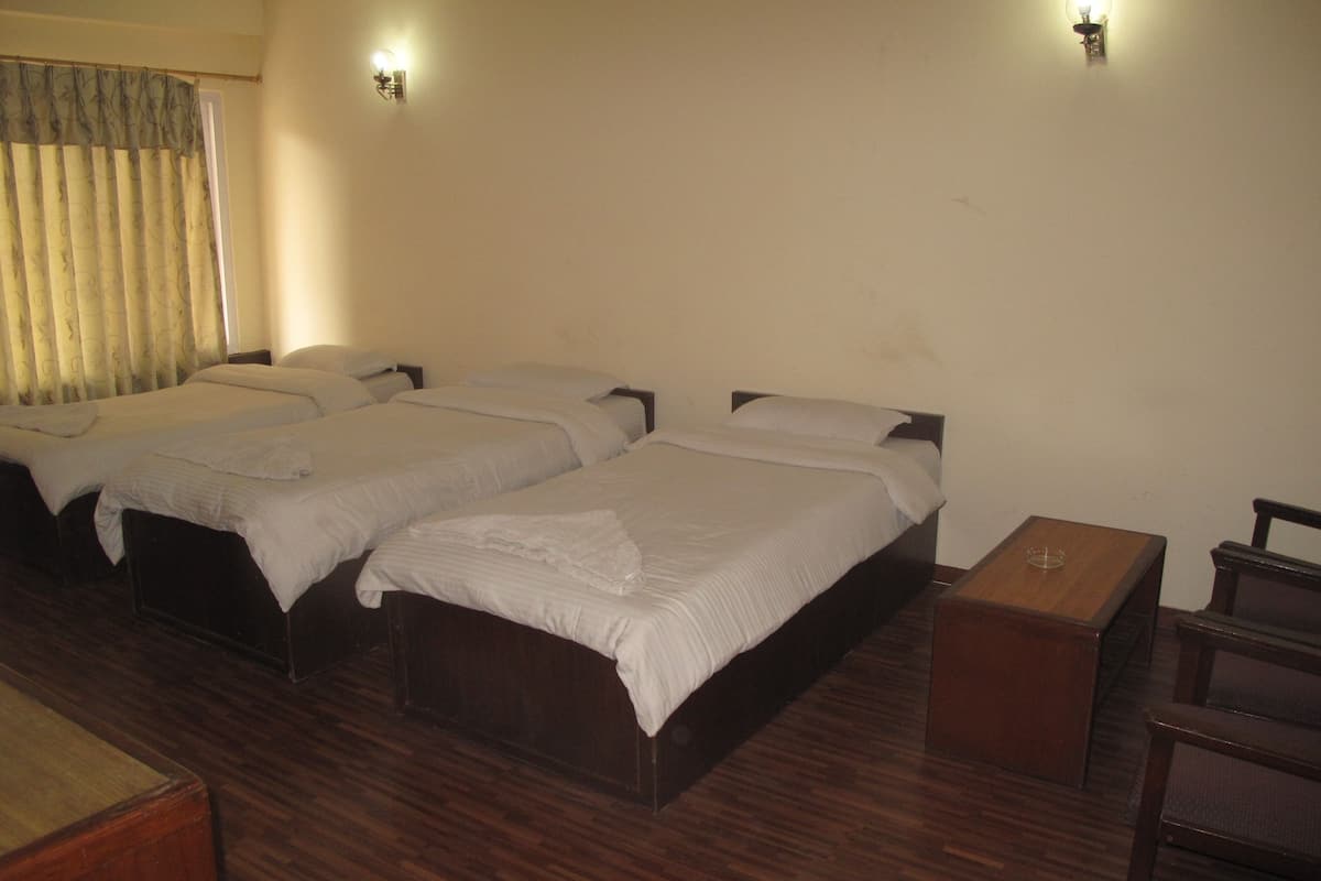 Ein Hotelzimmer mit drei Einzelbetten, Holzboden, einem kleinen Holztisch und einem Fenster mit Vorhängen.