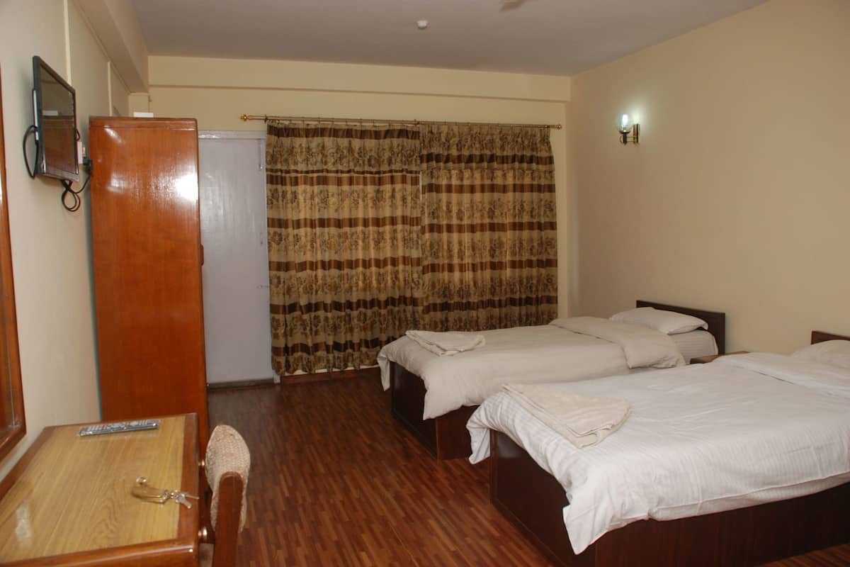 Ein Hotelzimmer mit zwei Betten, einem Holztisch, einem Kleiderschrank und einem Vorhang.