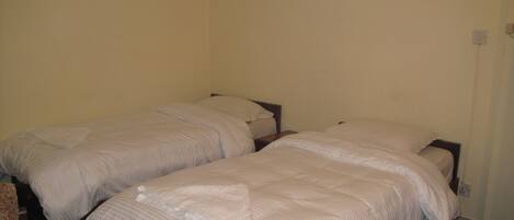Une chambre avec deux lits simples, chacun doté d’une tête de lit en bois et de draps blancs.