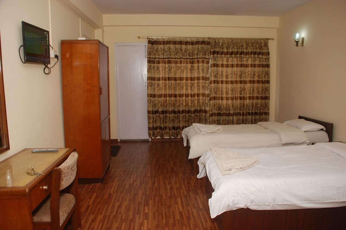 Ein Hotelzimmer mit Holztisch, Kleiderschrank, einem Bett mit weißer Bettwäsche, einem Vorhang und einer wandmontierten Lampe.