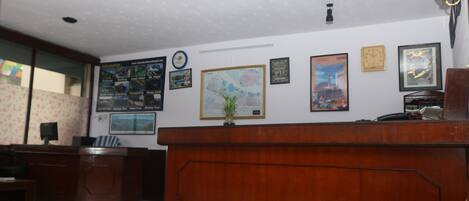 A reception desk with framed maps and certificates on the wall, a wooden desk, and a small plant on top.