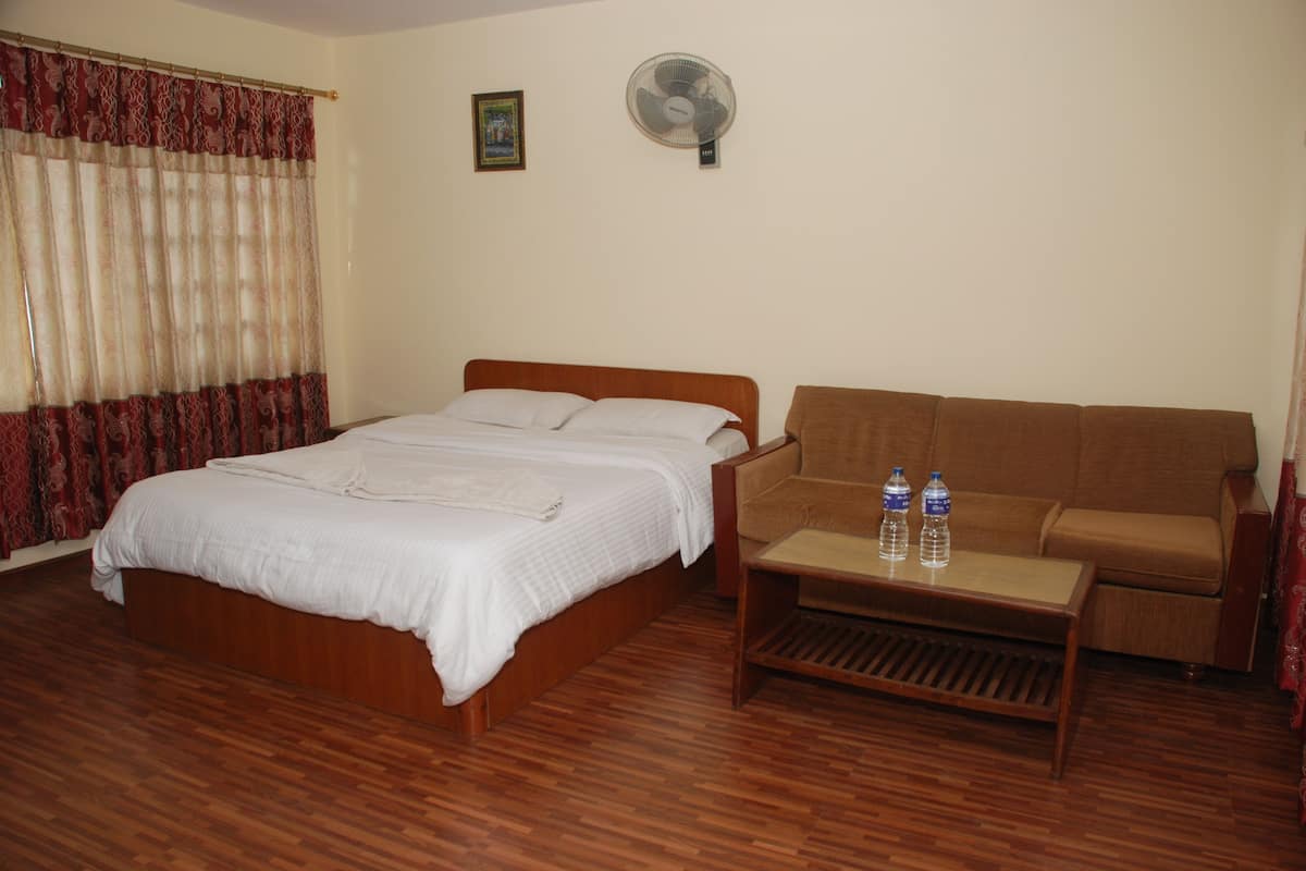 Ein Hotelzimmer mit einem hölzernen Bett, einem braunen Sofa, einem Holztisch und einem Standventilator.