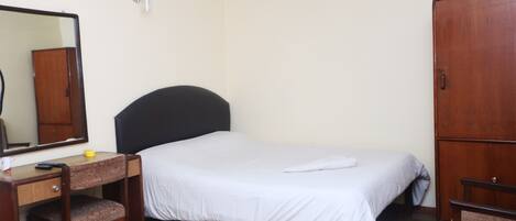 Un dormitorio con cama, escritorio, silla, armario, ventilador de techo y espejo.