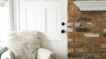 A room with a white door, a floral armchair, a brick wall, and a book on a shelf.