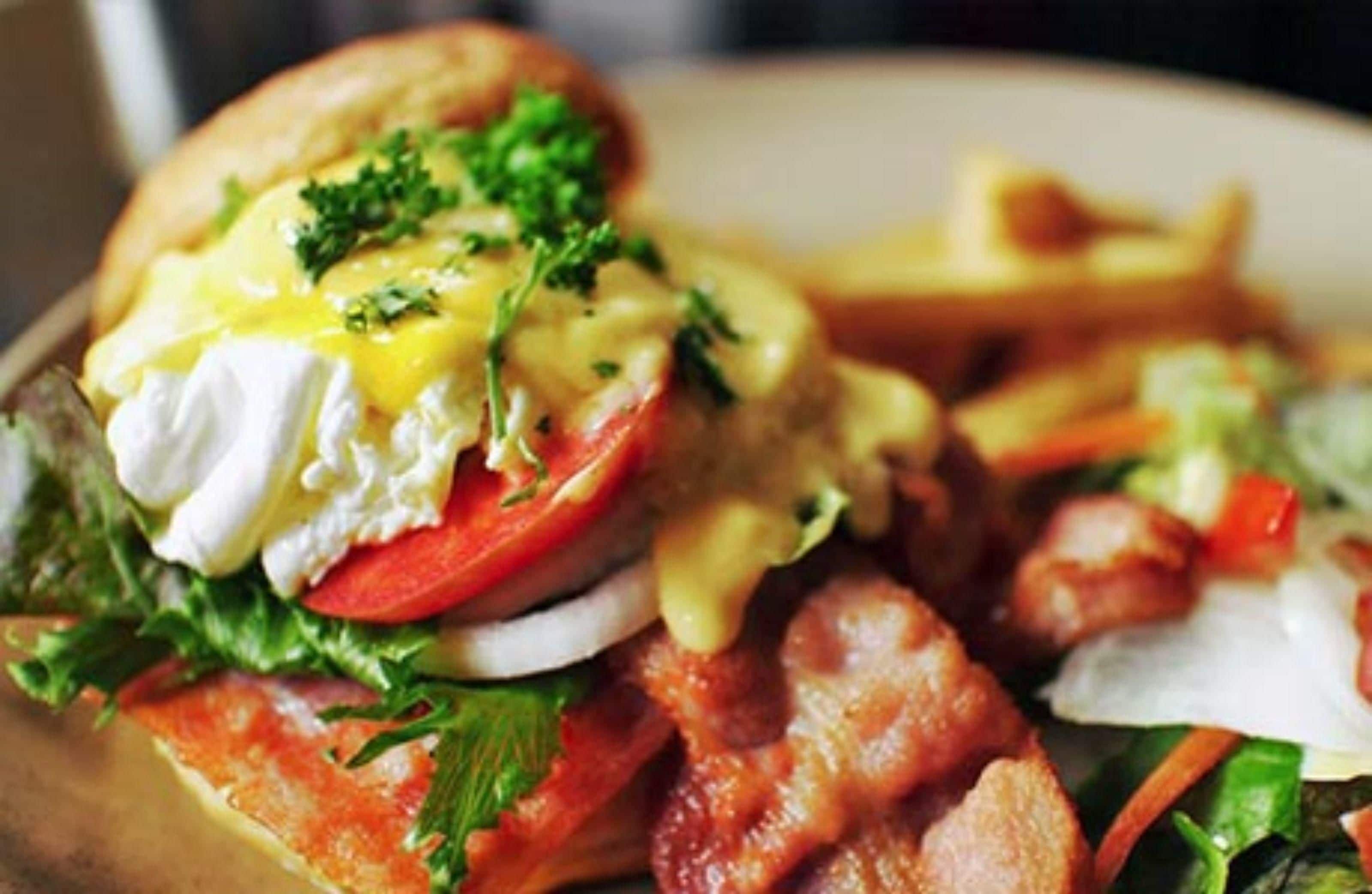 A close-up of a breakfast sandwich with egg, cheese, and greens, alongside a side of fries and salad.